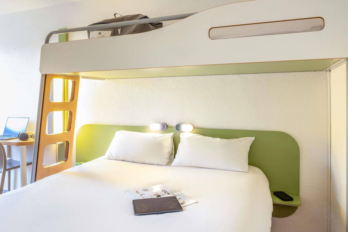 A bunk bed with a green headboard, a bedside table with a laptop, and a pillow on the lower bunk.