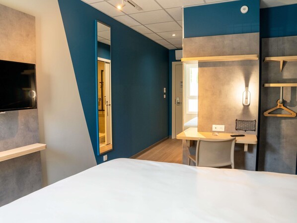 A hotel room with a bed, a desk, a chair, a TV, and a mirror.