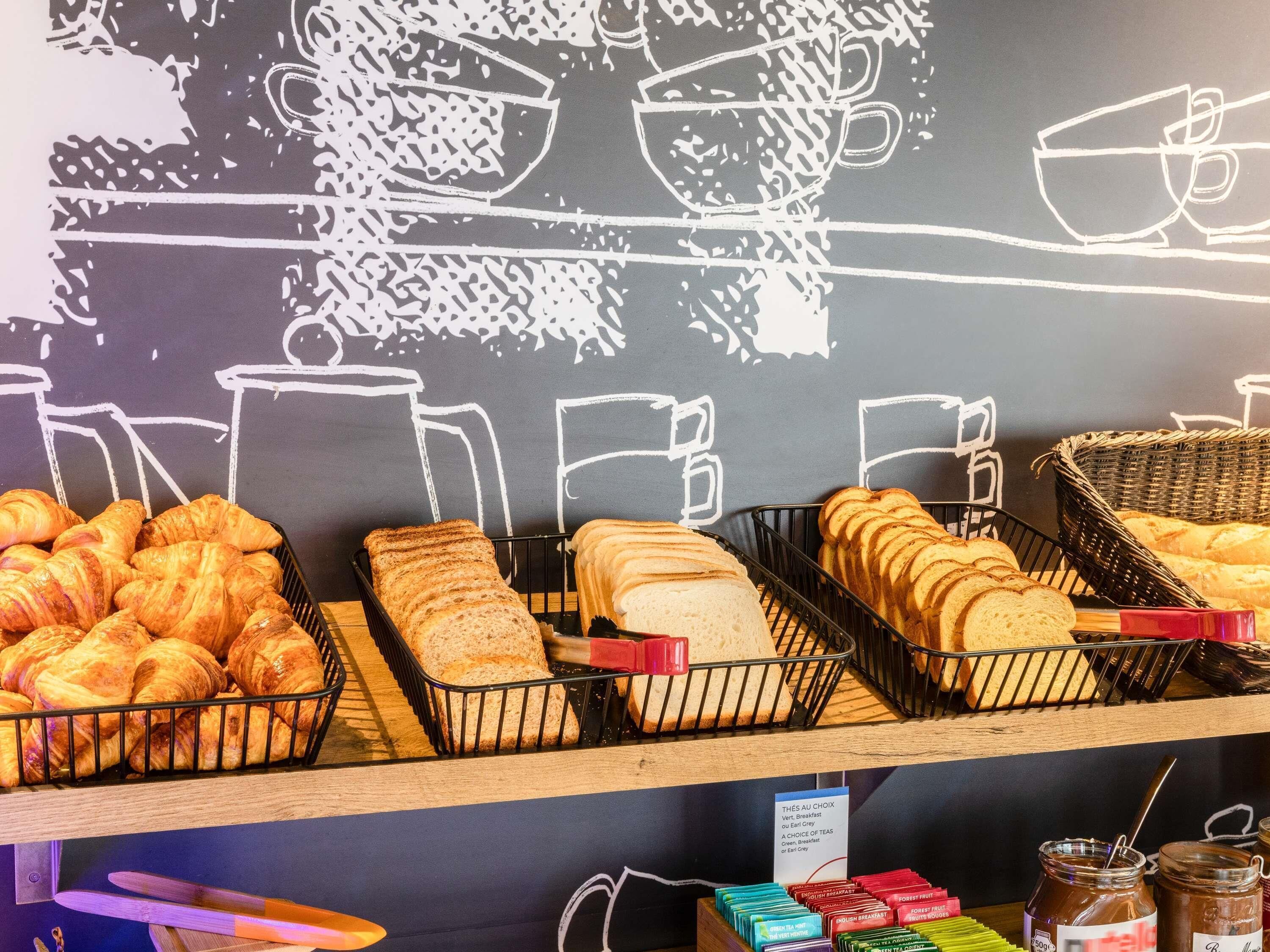 Eine Bäckerauslage mit Croissants, Baguettes und Brot, sowie Gläsern mit Marmelade und Tee.