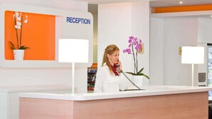 Un mostrador de recepción con un cartel que dice 'RECEPTION', una orquídea en maceta y un teléfono.