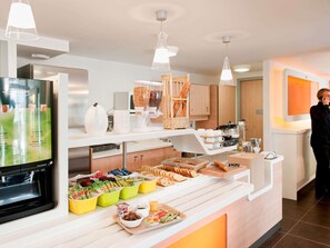 Ein Bereich mit Buffet, darunter ein Kühlschrank, eine Kaffeemaschine und verschiedene Speisen.
