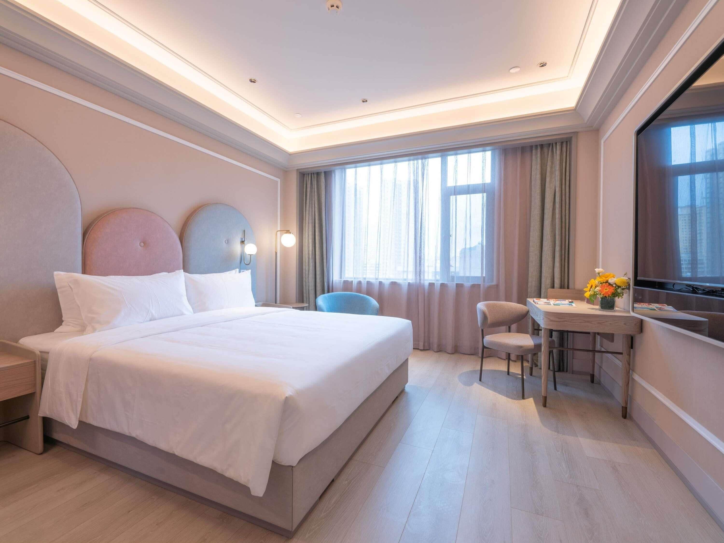 A hotel room with a large bed, a desk, a chair, and a TV.