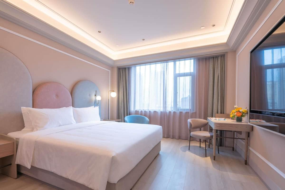 A hotel room with a large bed, a desk, a chair, and a TV.