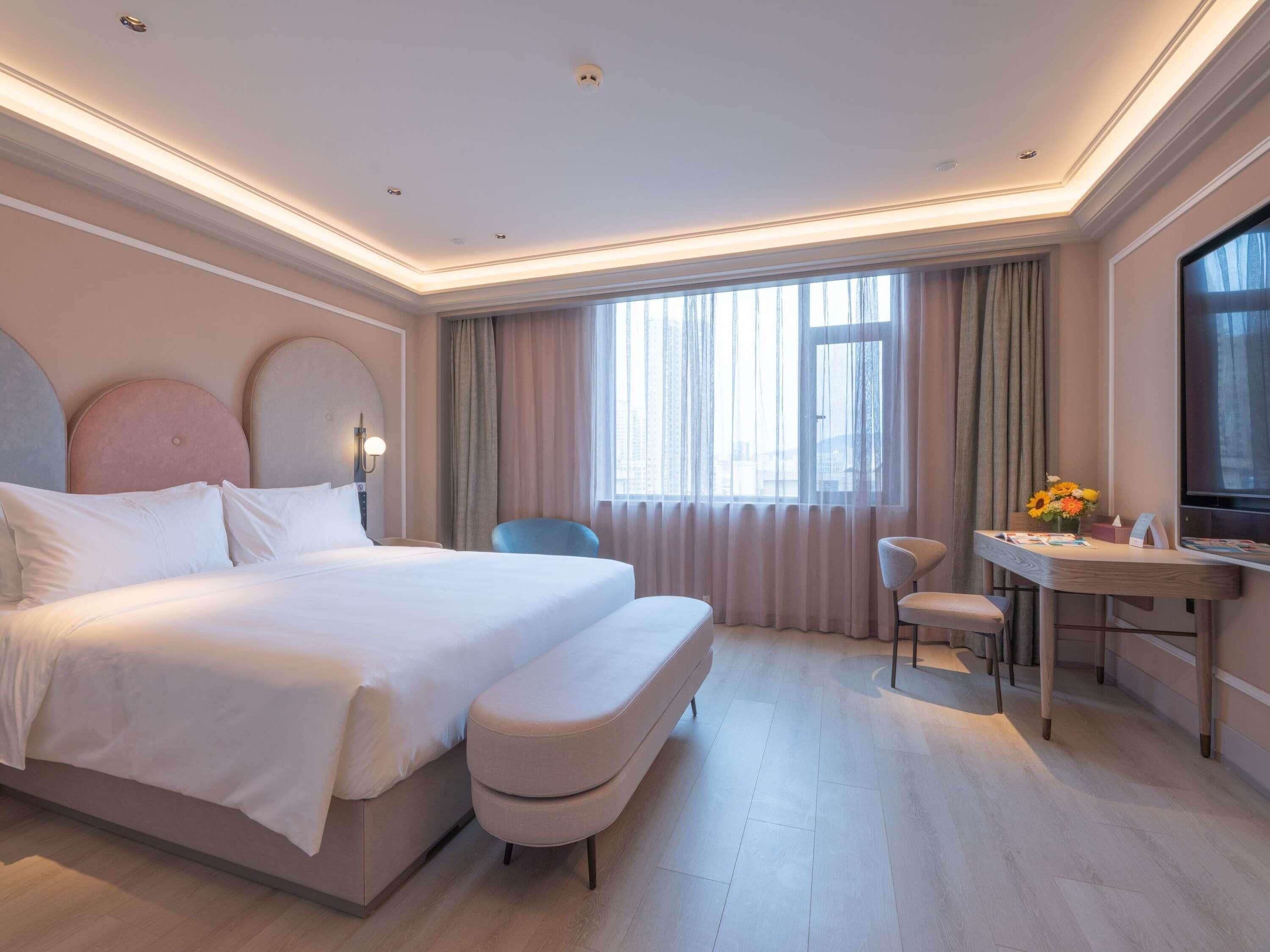 A hotel room with a large bed, a desk, a chair, and a TV.
