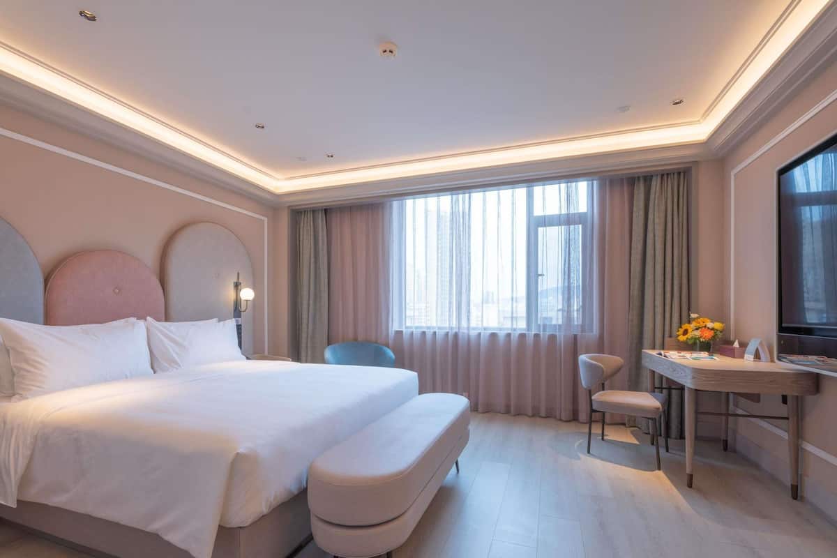A hotel room with a large bed, a desk, a chair, and a TV.