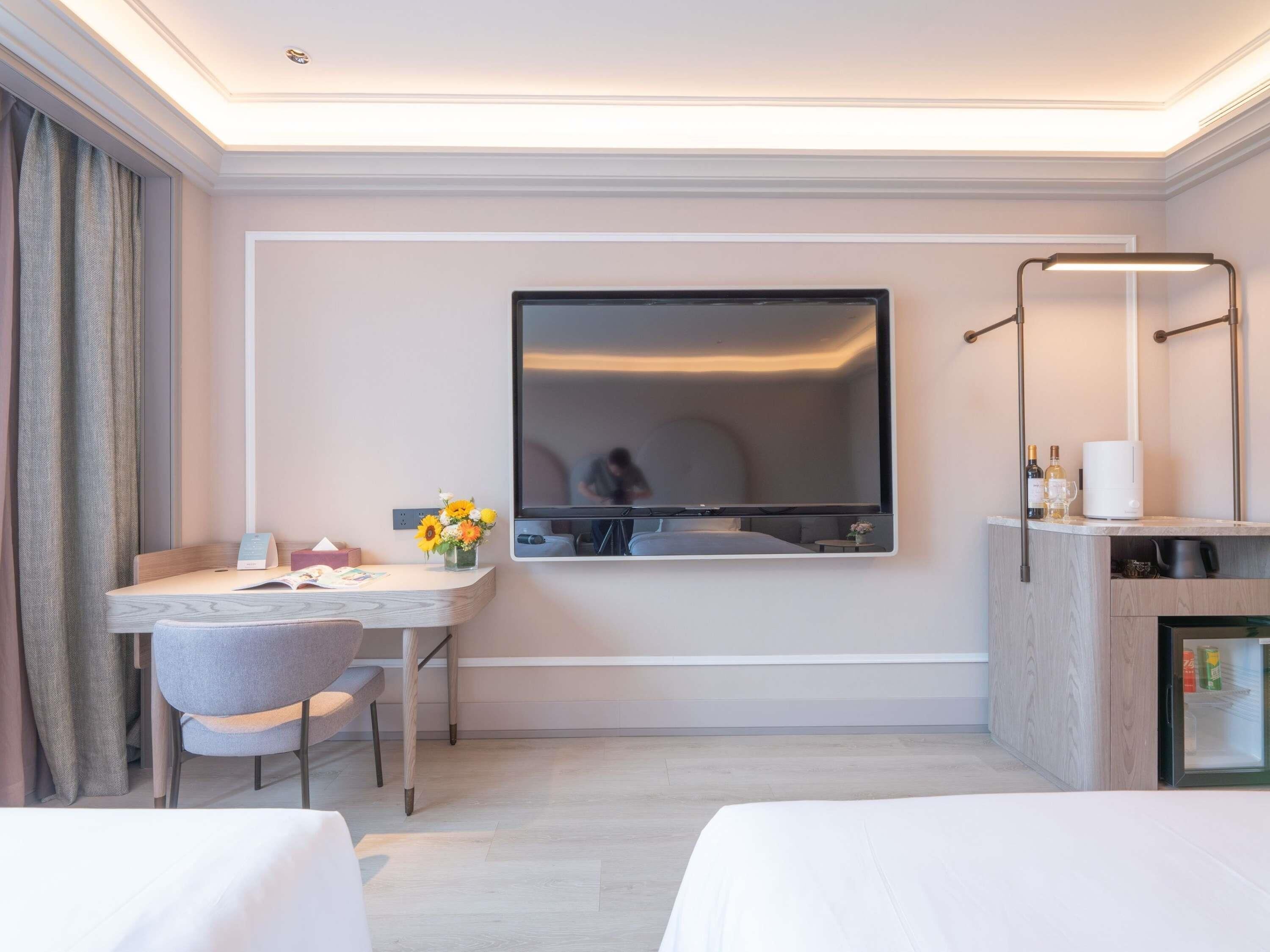 Ein Hotelzimmer mit einem Bett, einem Schreibtisch mit Stuhl, einem großen Spiegel und einer Minibar.