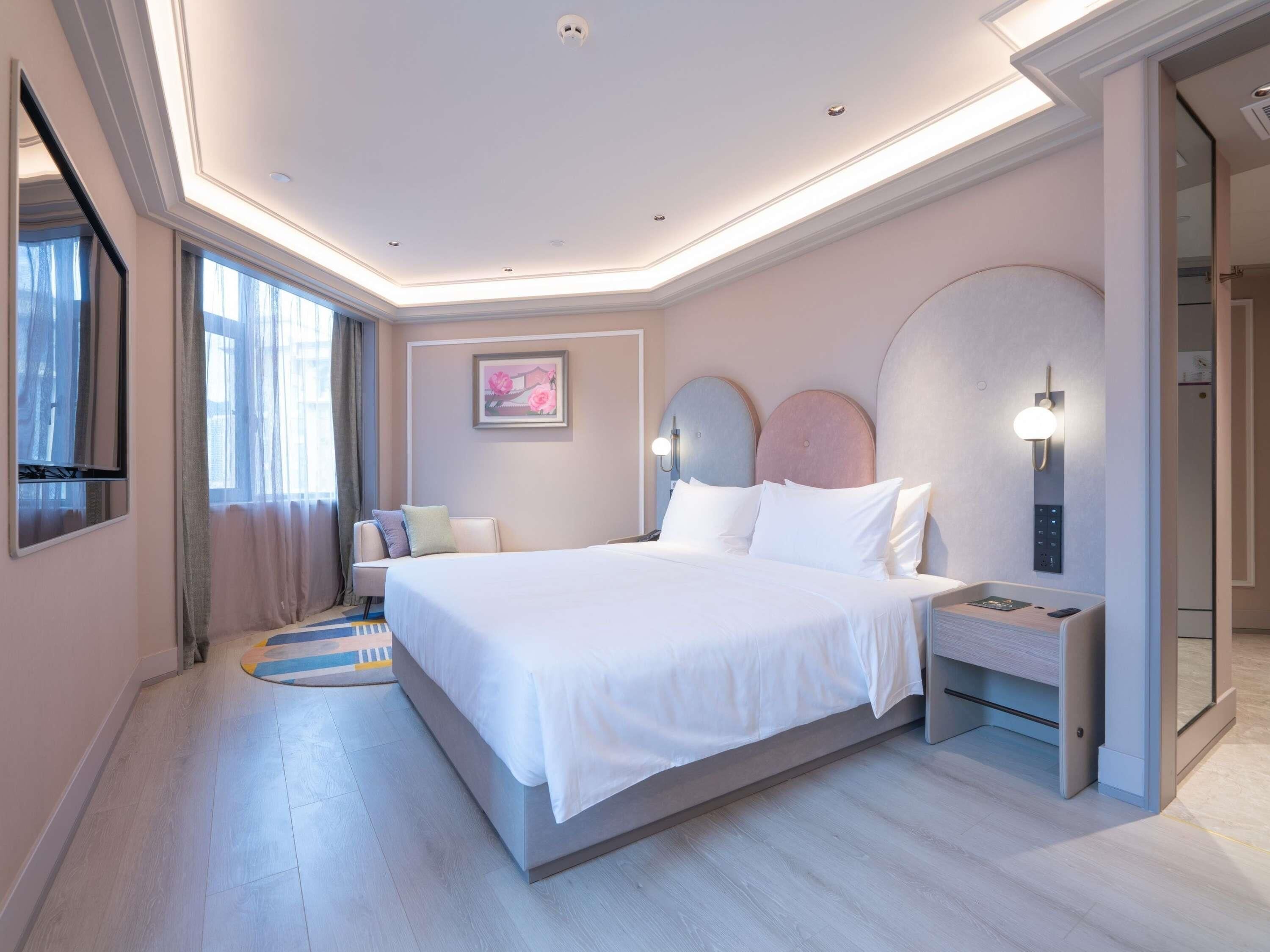 A modern hotel room with a large bed, bedside tables, a flat-screen TV, and a painting on the wall.