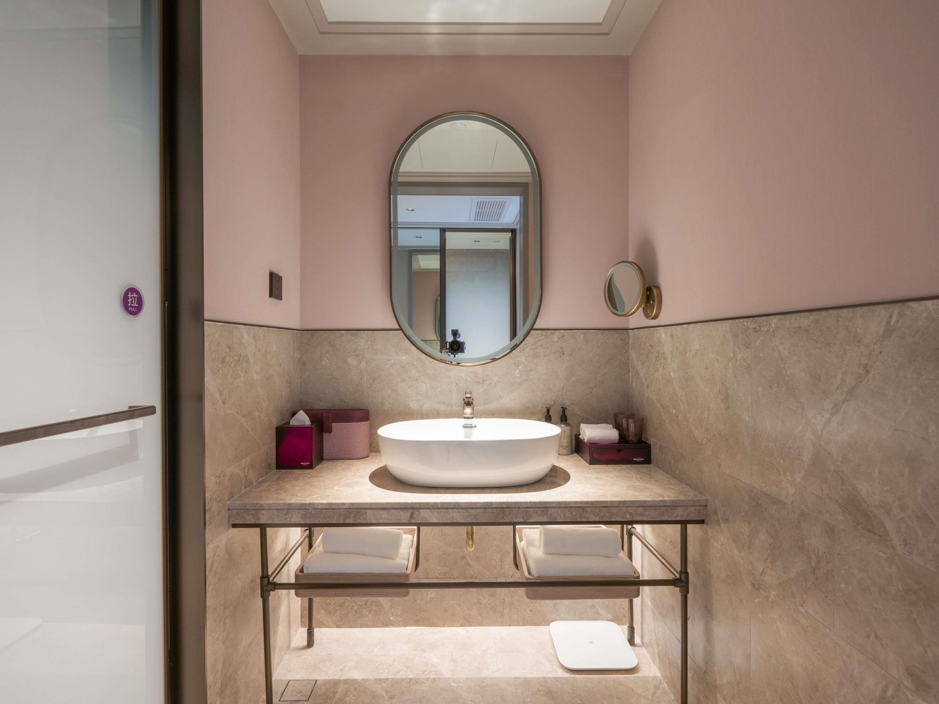 A bathroom with a large oval mirror, a round sink, and a vanity with a towel rack.