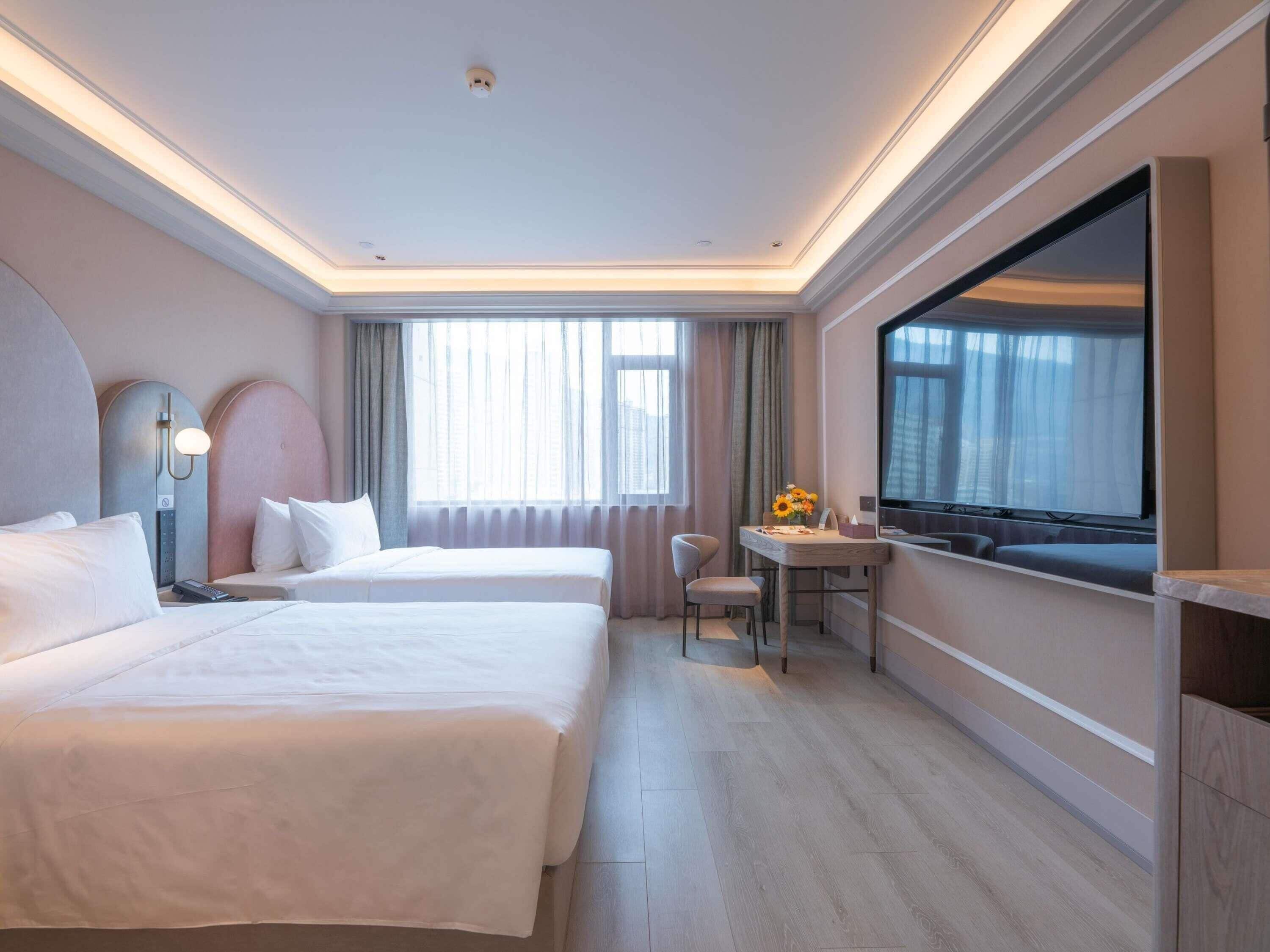 A hotel room with two beds, a desk, a chair, a TV, and a large window.