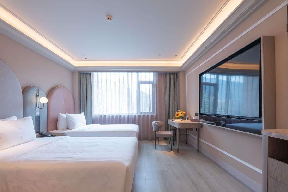A hotel room with two beds, a desk, a chair, a TV, and a large window.