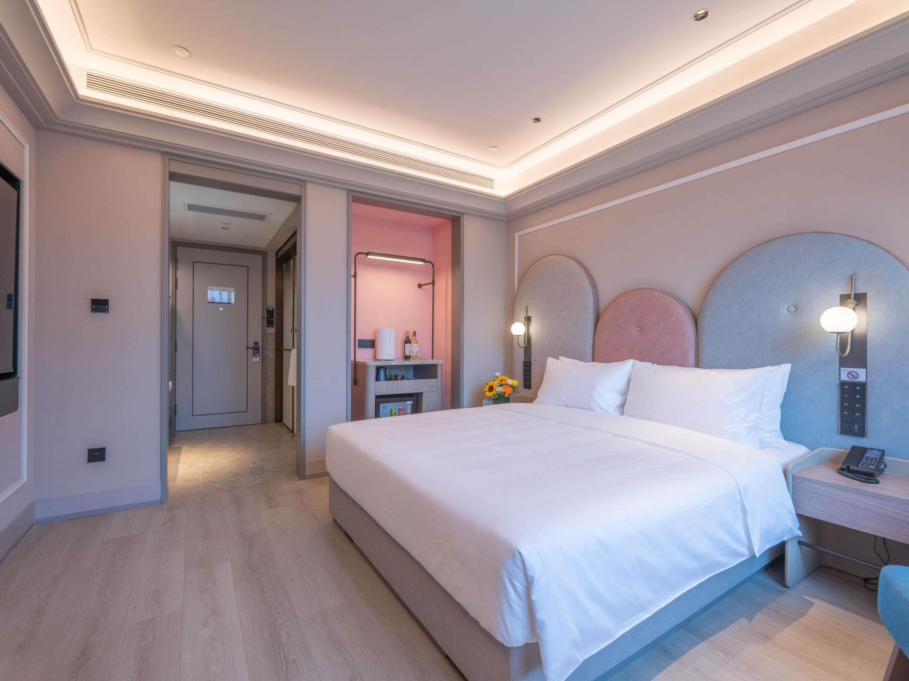 A hotel room with a large bed, bedside table, and a desk with a chair.