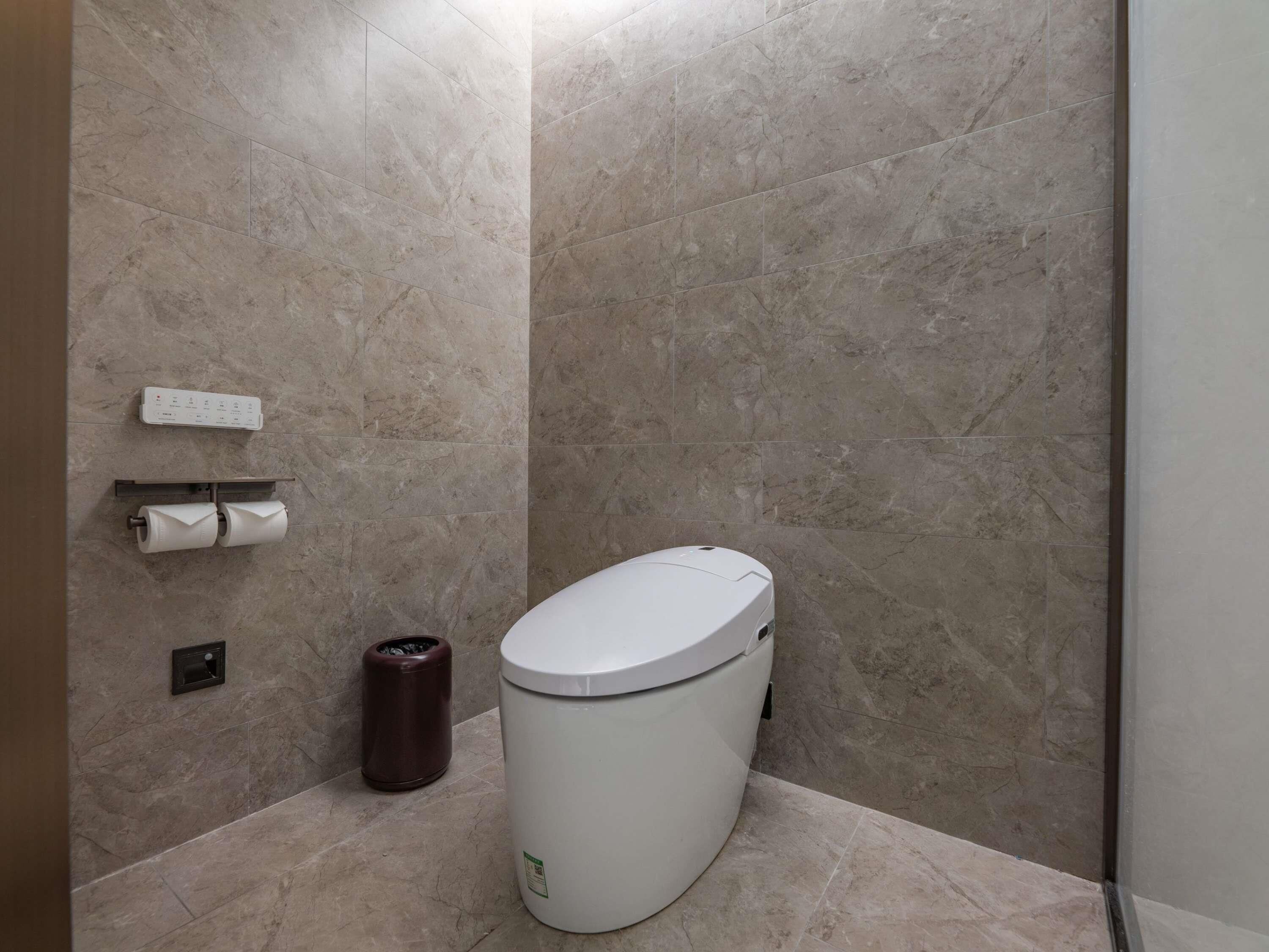 Un baño moderno con inodoro, un bote de basura y dispensador de toallas de papel.