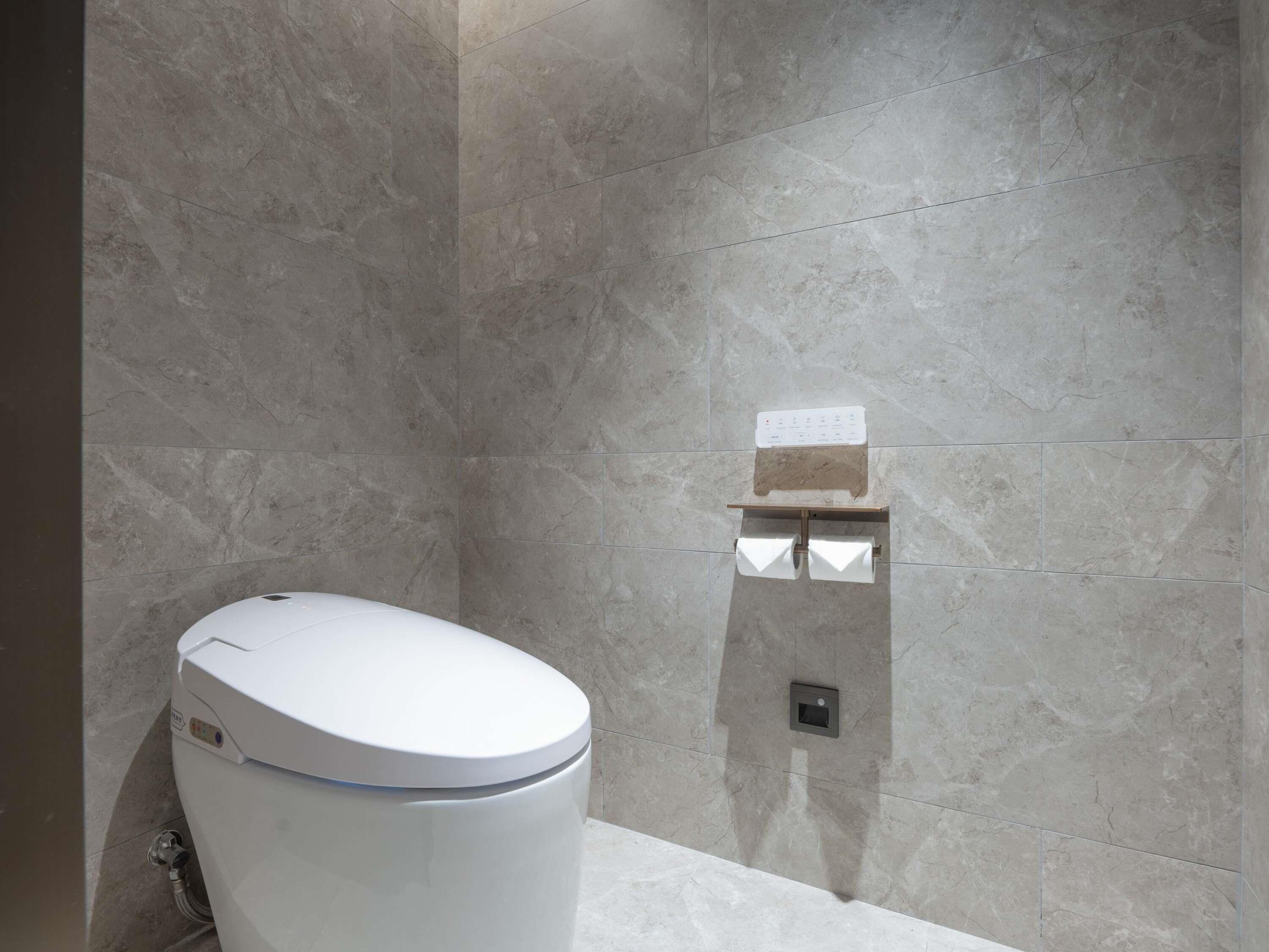 A modern bathroom with a toilet, a shower area, and a wall-mounted control panel.