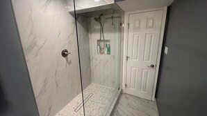 A modern bathroom with a glass-enclosed shower, marble walls, and a white door.