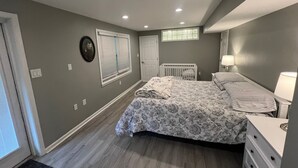 A bedroom with a bed, a crib, a dresser, a window with blinds, and a door.