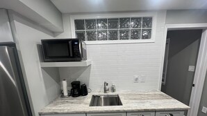 A kitchen with a stainless steel refrigerator, a microwave, a coffee maker, and a sink with a window above it.