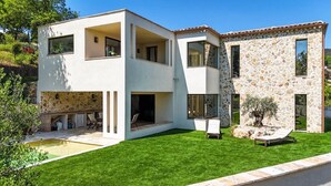 Una casa moderna de dos pisos con fachada de piedra, piscina y césped bien cuidado.