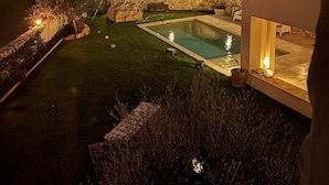 Un área de piscina moderna al aire libre con muros de piedra y un patio bien iluminado.