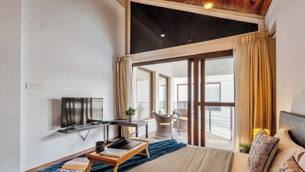 A hotel room with a bed, a desk, a laptop, a TV, and a balcony with a view. - Staymaster Water Wave 3BR Villa  (Vagator)