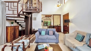 A living room with a staircase, a sofa, a coffee table with decorative items, and a dining area in the background. - Staymaster Water Wave 3BR Villa  (Vagator)