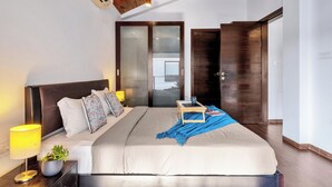 A bedroom with a bed, bedside lamp, bedside plant, and a wooden ceiling. - Staymaster Water Wave 3BR Villa  (Vagator)