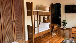 Habitación con literas, televisor, armario de madera y una mesita con toallas y libros.