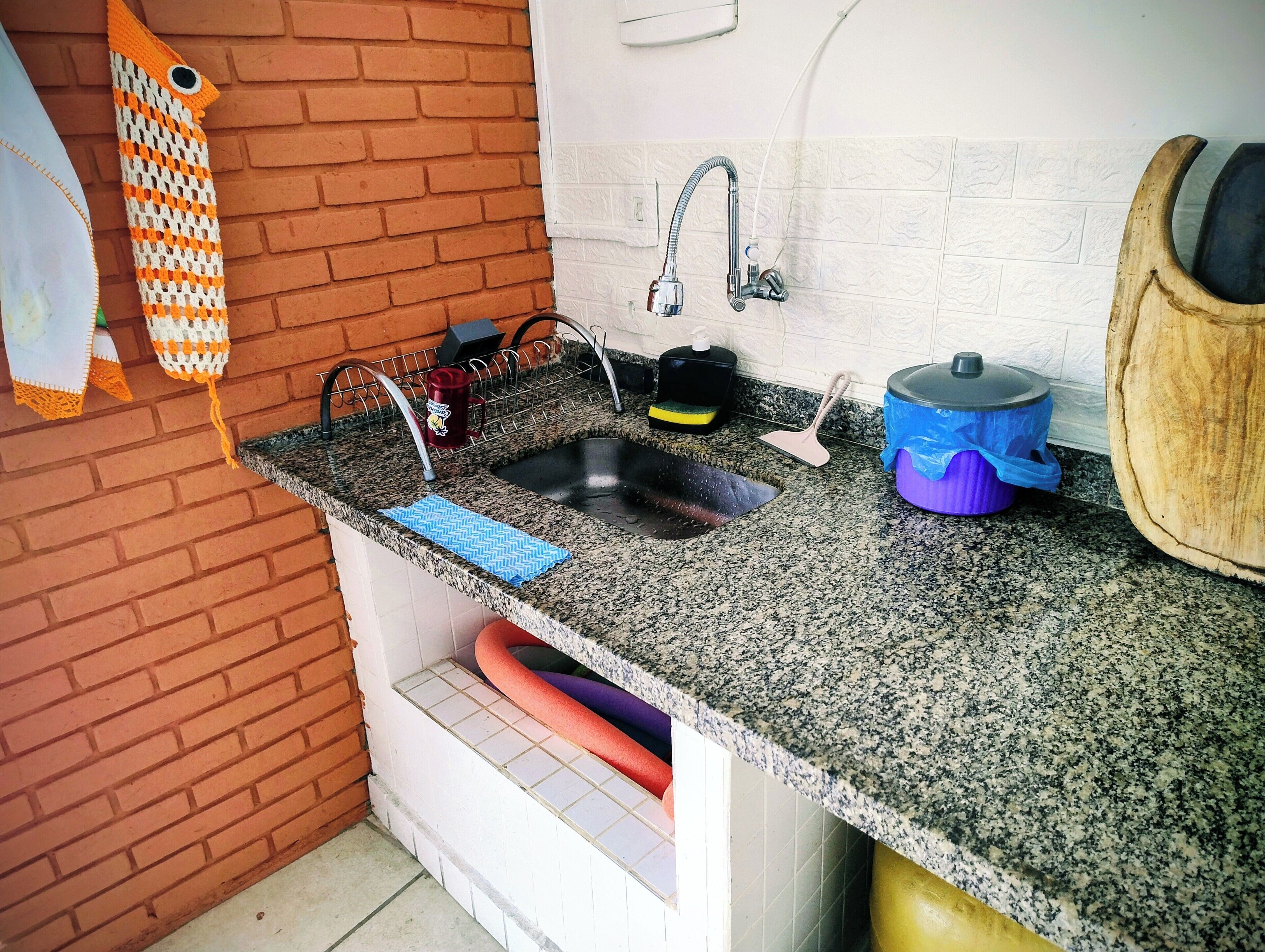 A kitchen with a granite countertop, a sink, a faucet, a dish rack, and a wooden cutting board.