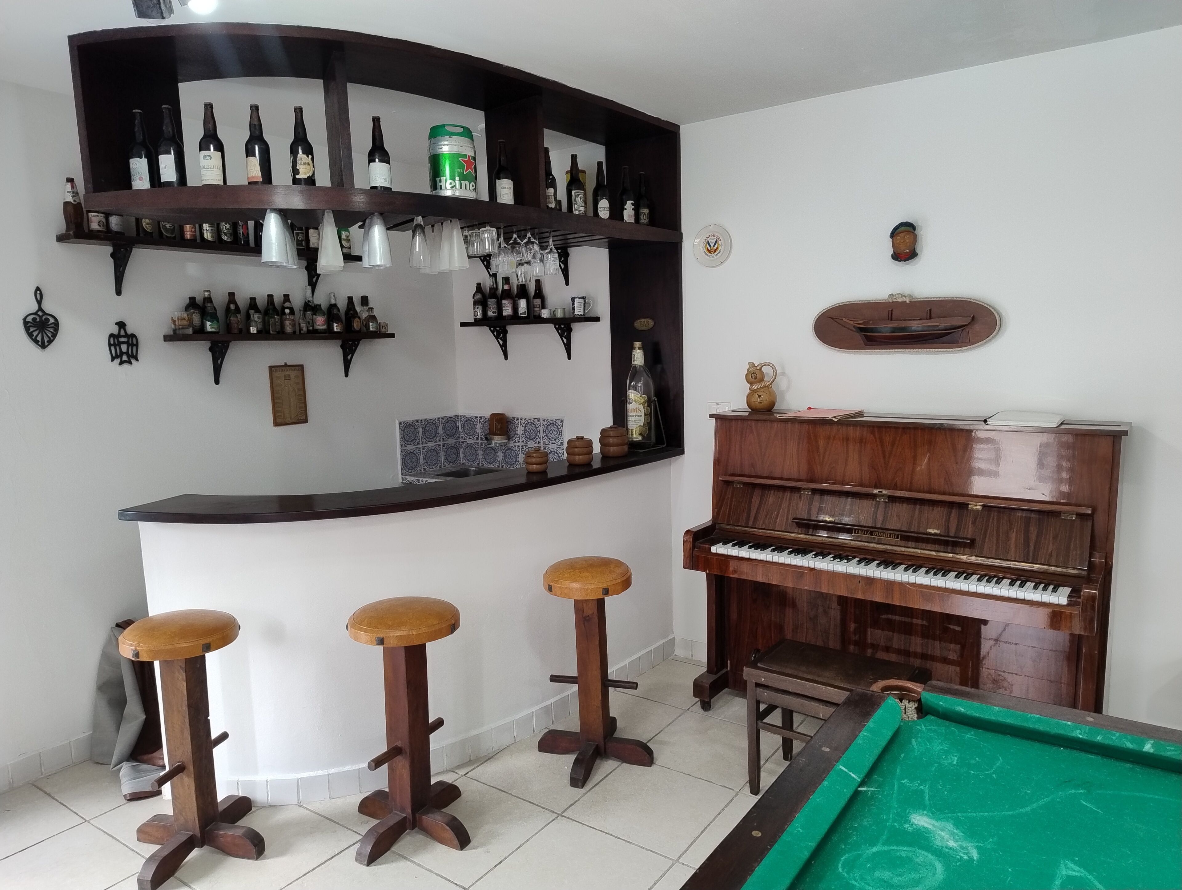 A bar area with shelves of bottles, a piano, stools, and a pool table.