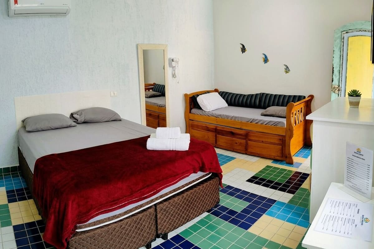 Una habitación con una cama, un banco de madera, un espejo y suelo de baldosas.