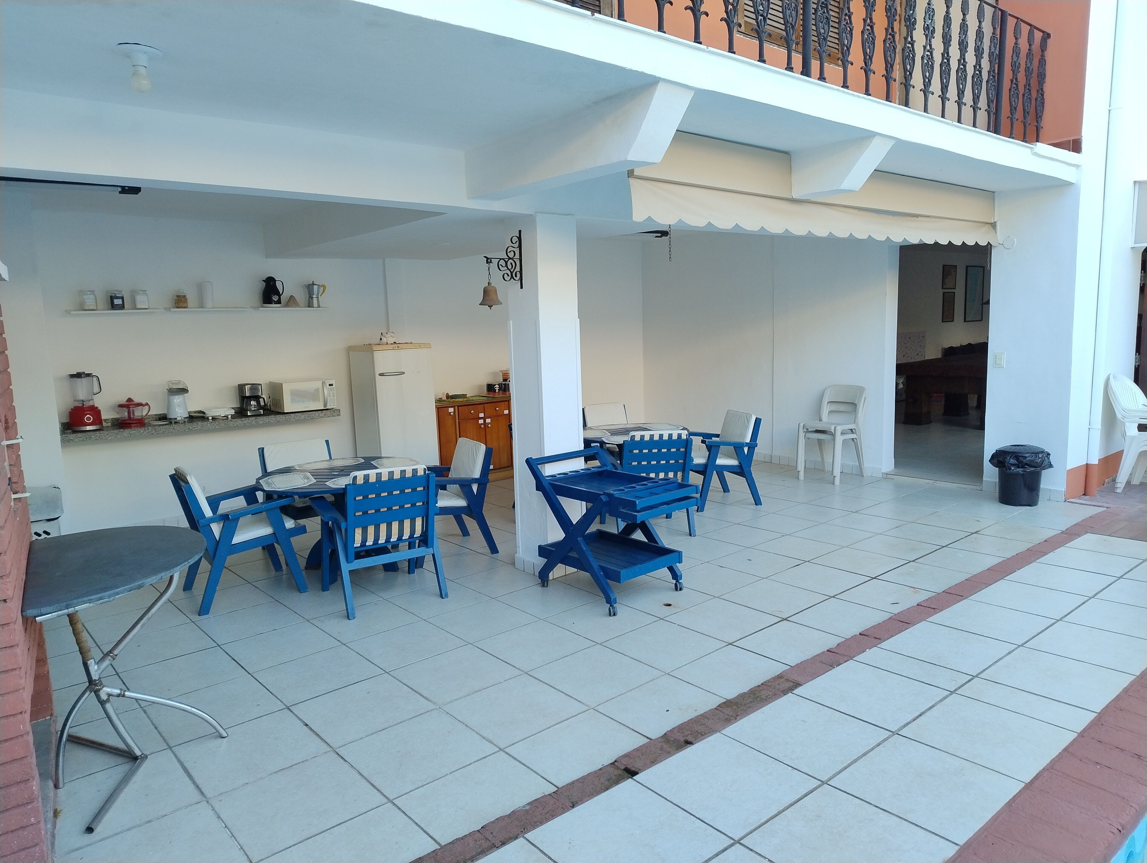 A dining area with blue chairs and a table, a kitchen with white cabinets, and a balcony with a white railing.