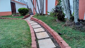 Un camino que conduce a un edificio con un borde de ladrillo rojo, un arbusto pequeño y un árbol.