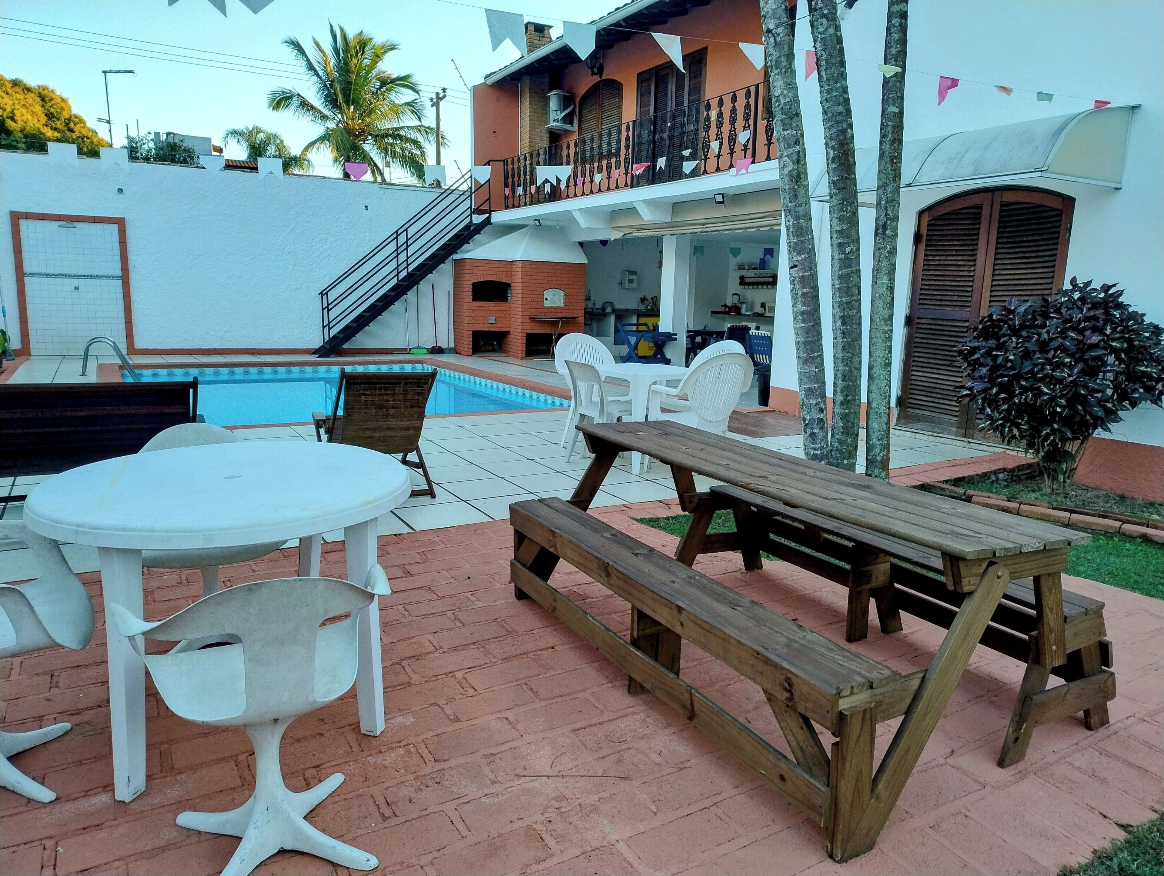 A pool area with a table and chairs, a wooden bench, and a staircase leading to a balcony.