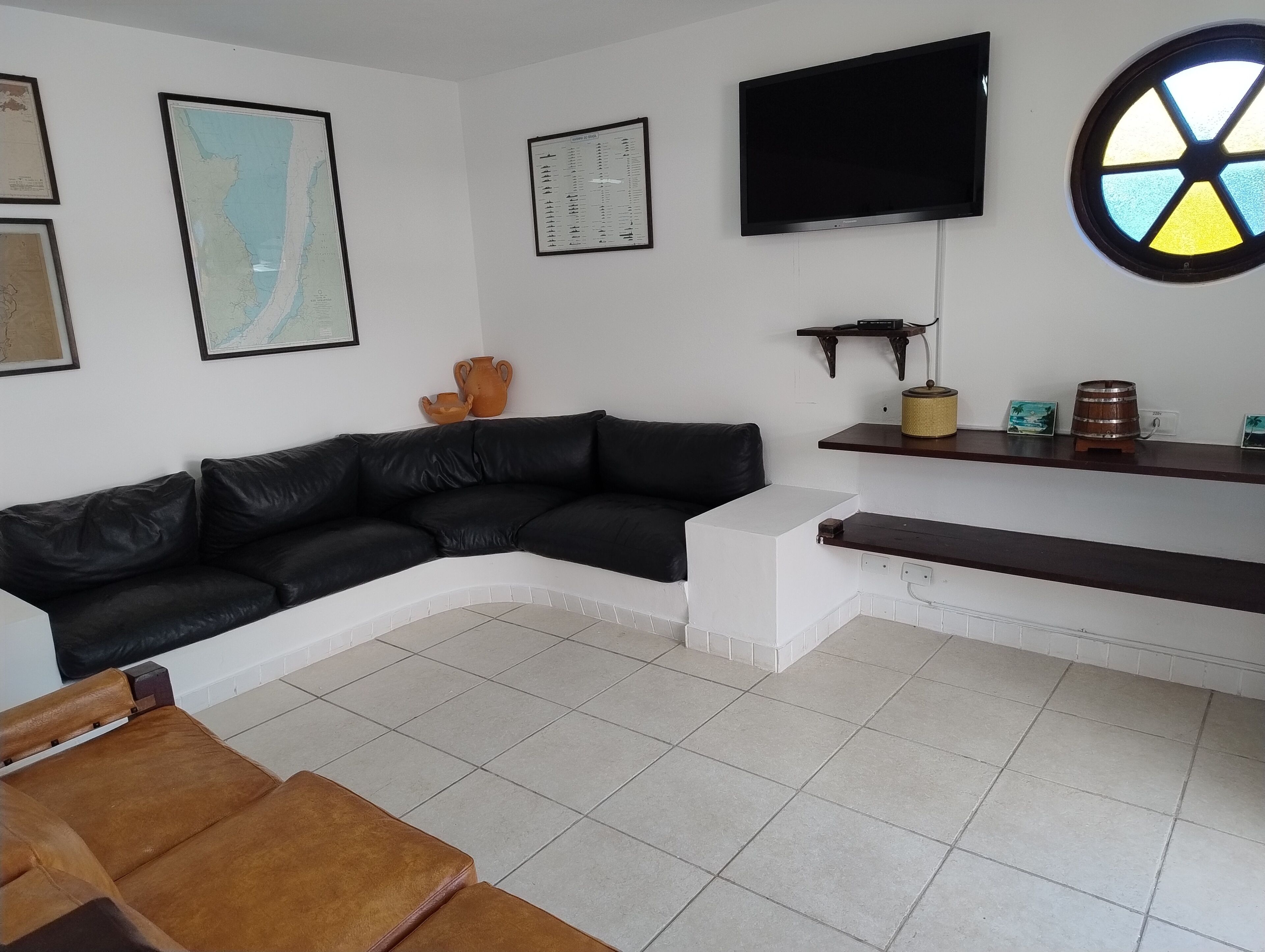 A living room with a black leather sofa, a white coffee table, a flat-screen TV mounted on the wall, and a small shelf with decorative items.