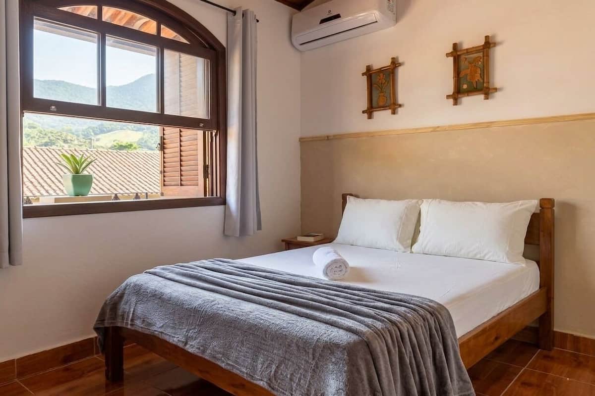 Un dormitorio con cama, ventana con vistas, aire acondicionado de pared y una mesita de noche.