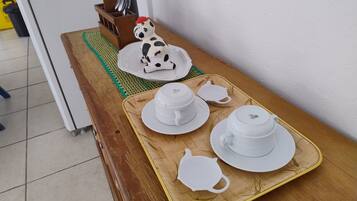 Una mesa de madera con una bandeja que sostiene tazas y platillos blancos, un calentador de té y una pequeña figurita de vaca.