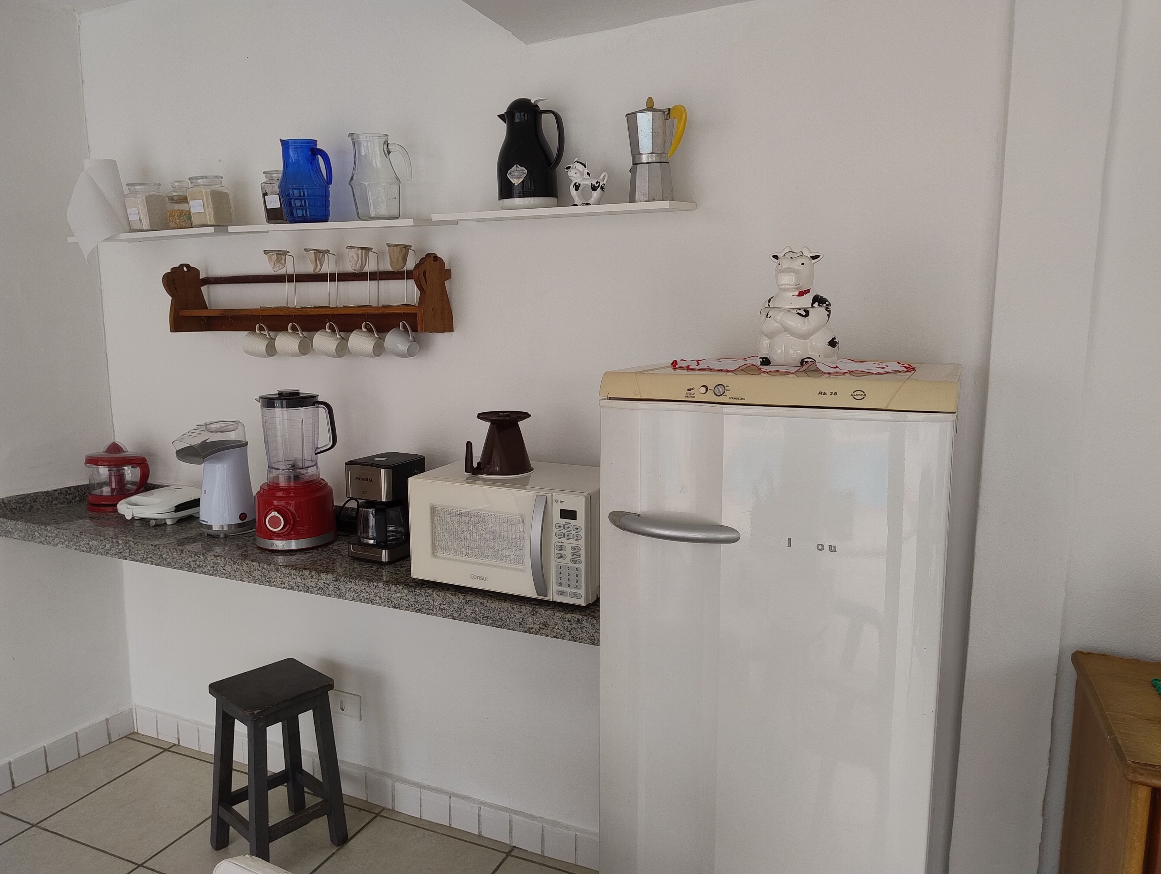 A kitchen with a refrigerator, microwave, coffee maker, blender, and various kitchen utensils.