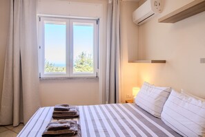 A hotel room with a bed, a window with curtains, a bedside lamp, and an air conditioning unit. - Attico Asinara è situato al piano superiore di una villa immersa nel verde (Marina di Sorso)