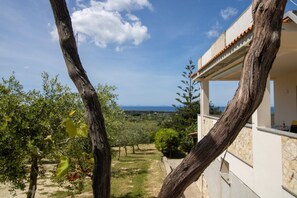 A villa with a stone exterior, a balcony, and a view of a vineyard and distant mountains. - Attico Asinara è situato al piano superiore di una villa immersa nel verde (Marina di Sorso)