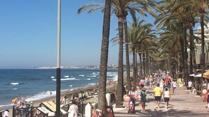 Eine Küstenpromenade gesäumt von Palmen, ein Strand und eine Menschenmenge.