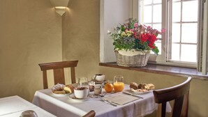 Una mesa de desayuno con diversos pasteles, una taza de café, un vaso de jugo de naranja y una cesta de flores.