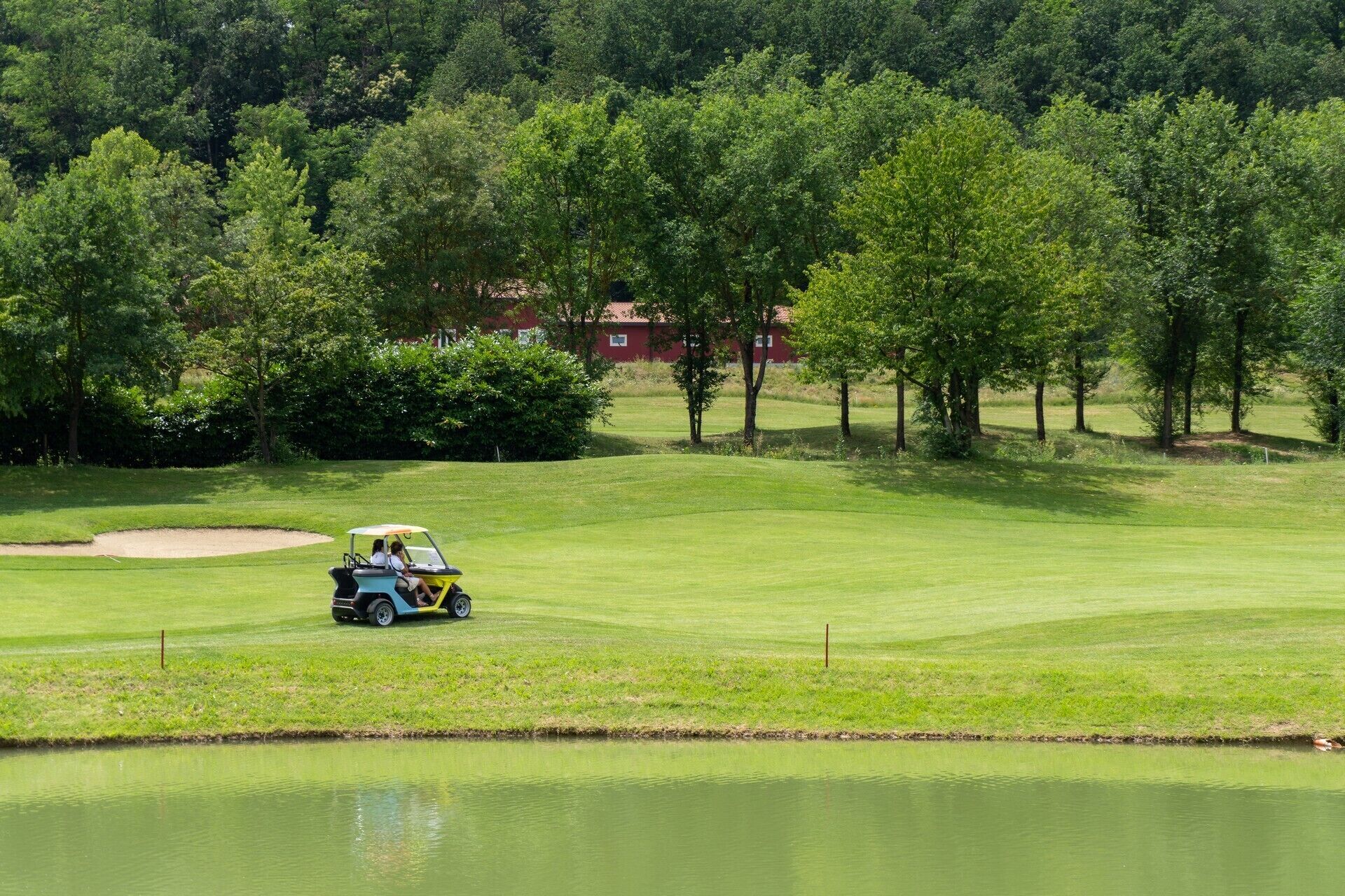 Un parcours de golf avec un obstacle d’eau, des arbres et un bâtiment en arrière-plan.