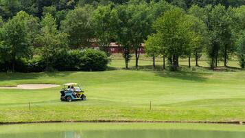 Ein Golfplatz mit einem Wasserhindernis, Bäumen und einem Gebäude im Hintergrund.