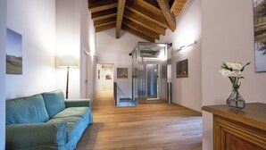 Un pasillo con piso de madera, un sofá verde, una lámpara, un jarrón con flores y una puerta que da a otra habitación.