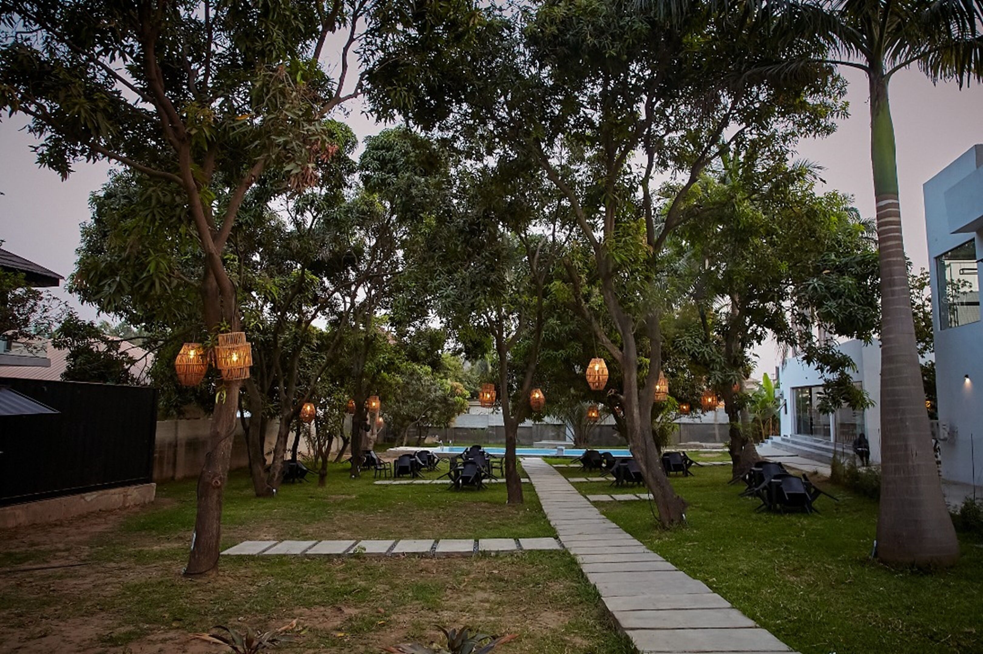 Un espace jardin aménagé avec des allées, des arbres, des sièges extérieurs et des éclairages décoratifs.