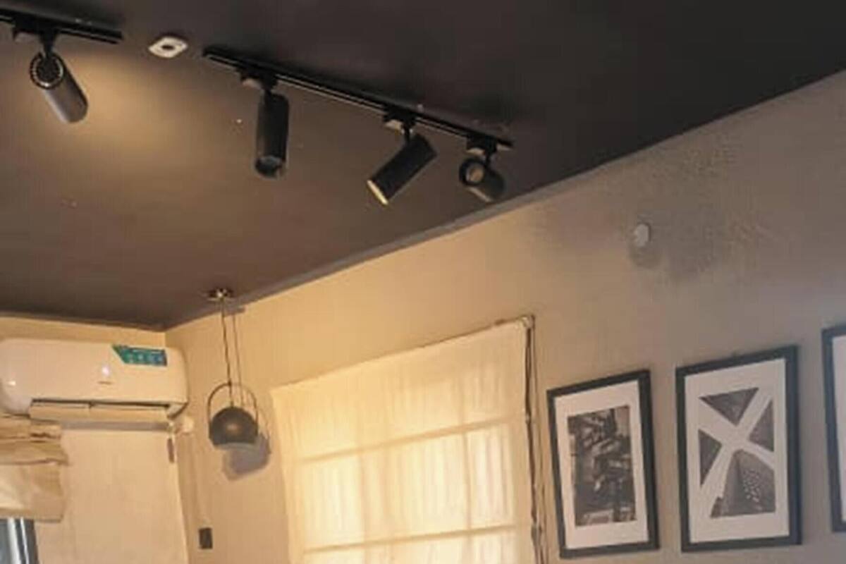 Une chambre à coucher avec un lit, un ventilateur sur pied, une fenêtre avec des rideaux et un climatiseur fixé au mur.