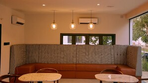 A modern interior with a brown sofa, two round tables, pendant lights, and an air conditioning unit. - SeaLord Resort Karu (Abuja)