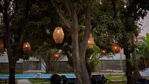 An outdoor seating area with wicker hanging lights, a pool, and lounge chairs. - SeaLord Resort Karu (Abuja)