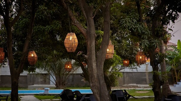 An outdoor seating area with wicker hanging lights, a pool, and lounge chairs. - SeaLord Resort Karu (Abuja)