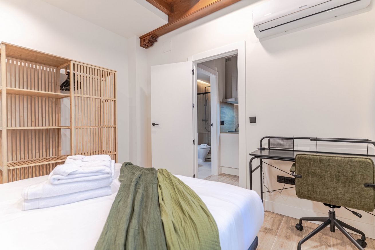 Quarto com cama, guarda-roupa de madeira, escrivaninha com cadeira e ar condicionado.