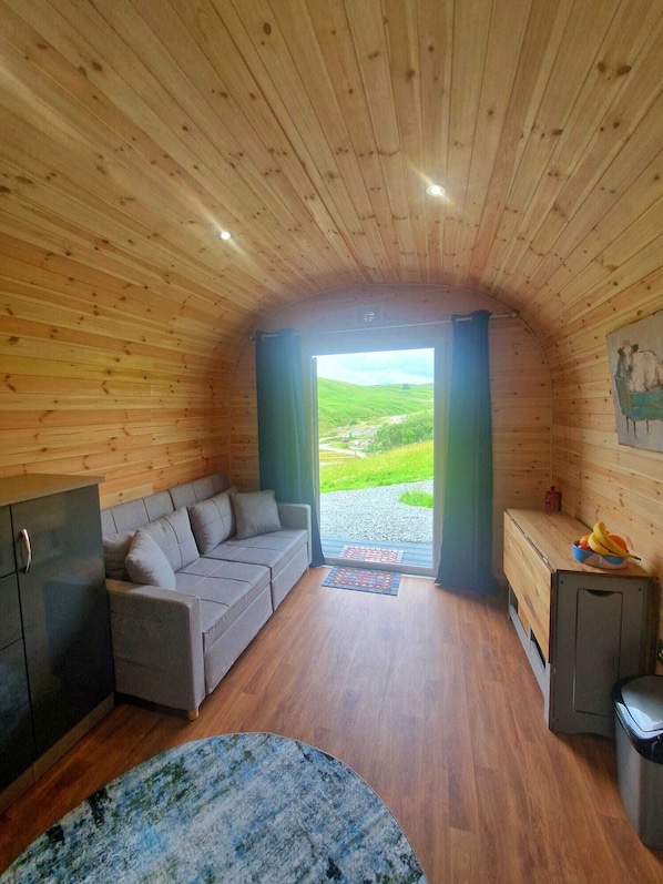 A cozy cabin interior with a sofa, a small table, and a view of a green landscape through a doorway. - The Star Inn (Llanbrynmair)